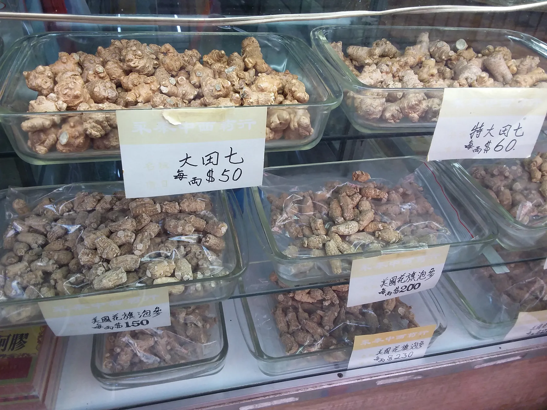 Trays of dried Panax notoginseng roots labelled tianqi and priced by the tael in a Kowloon City herb shop